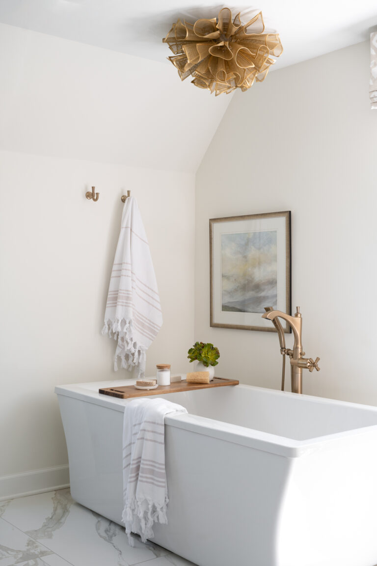 A large square bathtub is stationed on marble tiles with a freeform golden light fixture above.